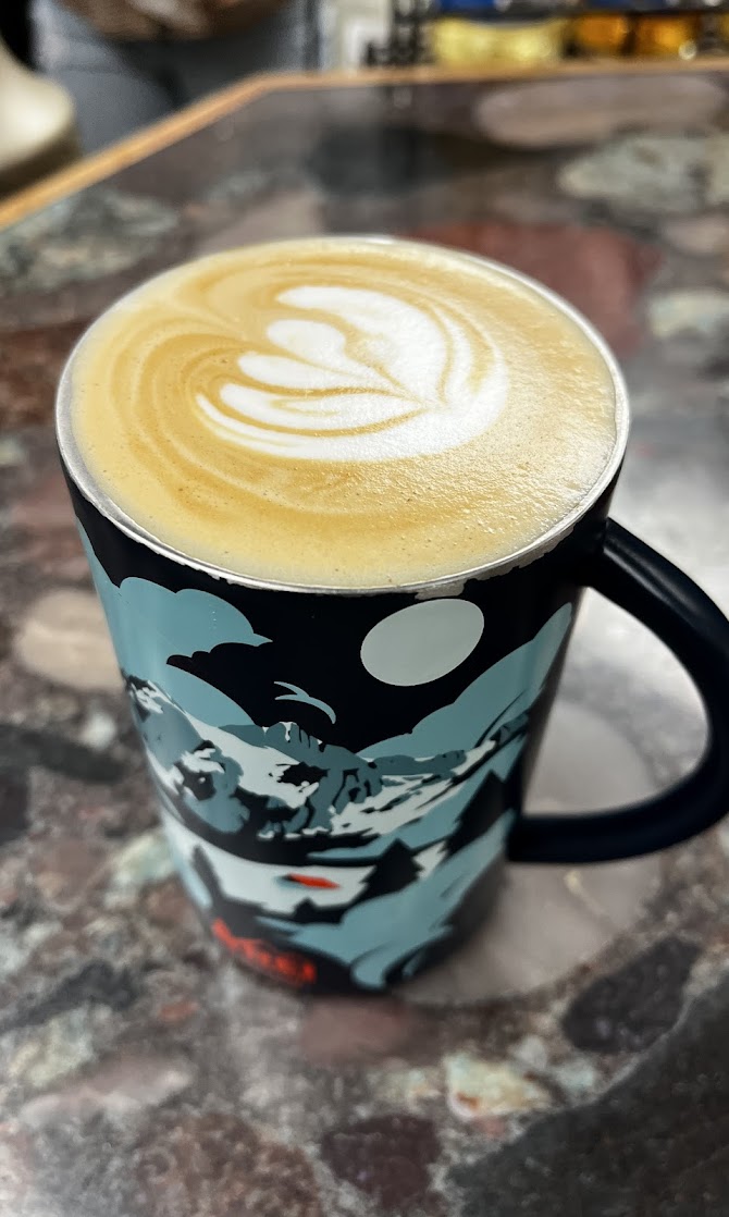 A latte with tulip latte art served in a mountain-scene mug at The Grind Coffee House